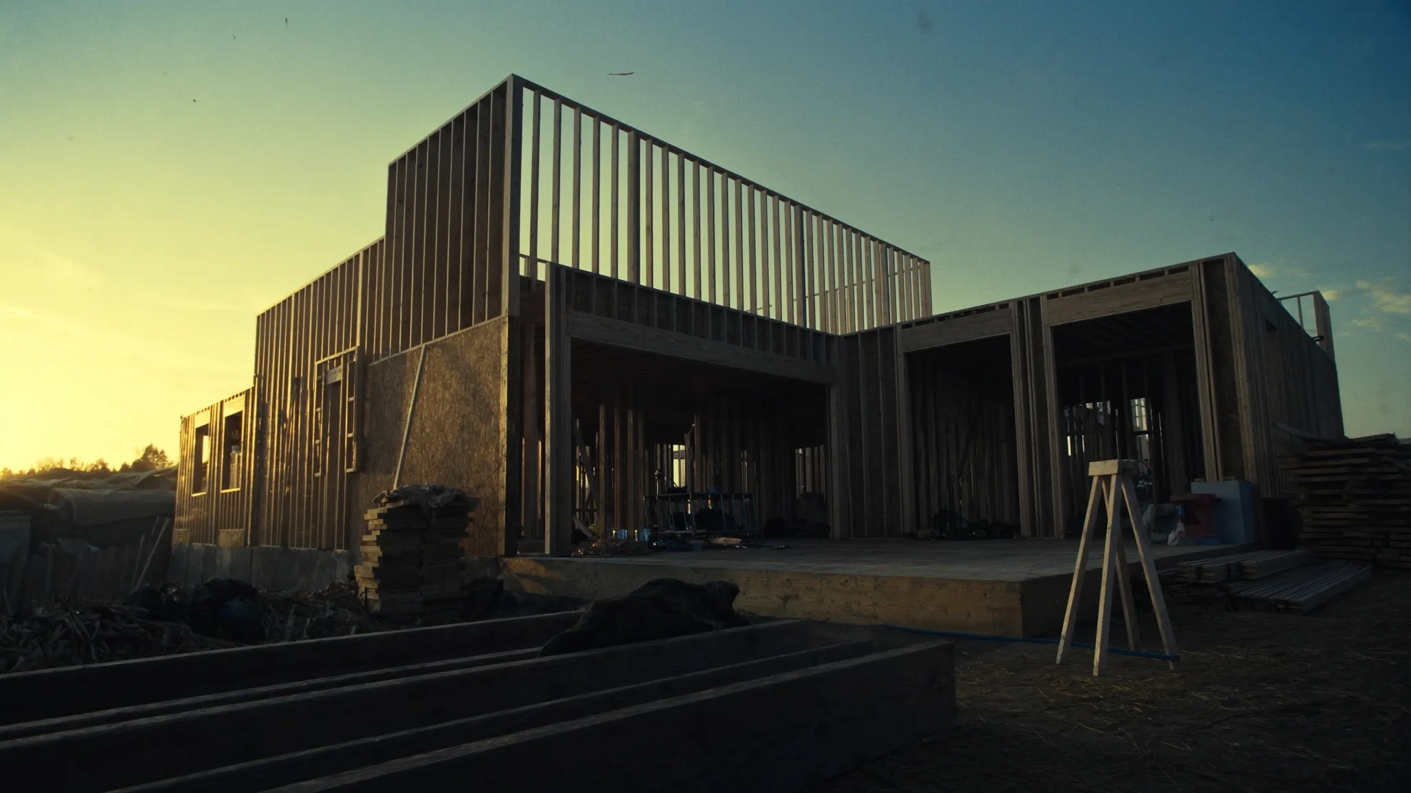 Golden-hour light streaming through the freshly framed walls of a two-storey home addition